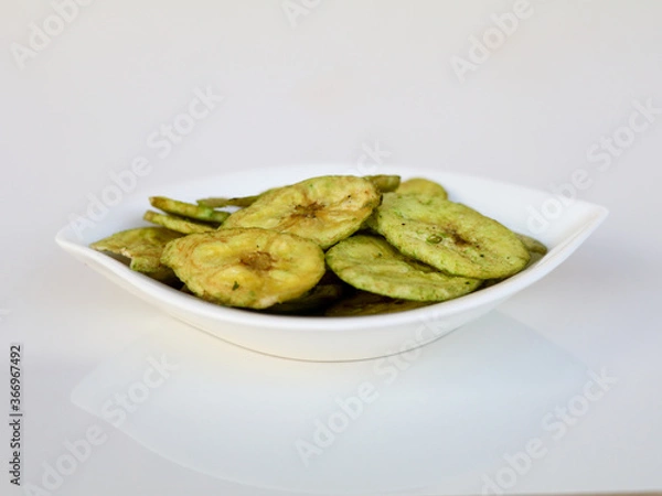 Fototapeta Green color banana chips with hot green chili flavor in a white bowl against white background