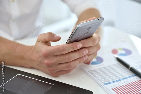 Fototapeta Businessman with mobile phone analyzing at graph and checking business plan.