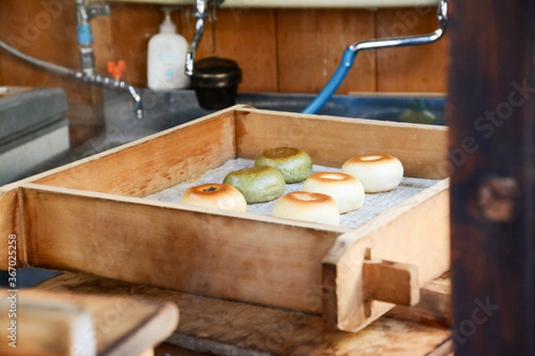 Obraz 信州の宿場町のおやき屋の店先で蒸しあがった、焼き目のついた白とよもぎの緑色のおやき
、木枠の蒸し器。台所。調理場、水道。