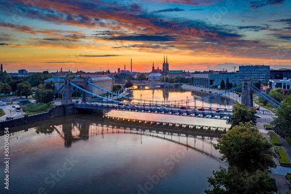 Fototapeta Drone view on the Grunwaldzki Bridge above Oder river in Wrocław at beautiful sunset. Rushing traffic, illuminated historic buildings and bridges. Beautiful sky, light reflections on the blurry water