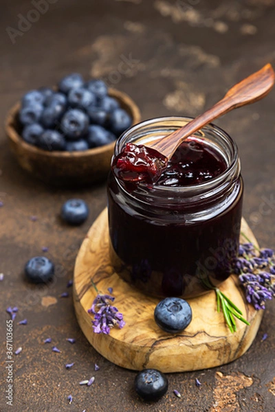 Obraz Glass jar and spoon with delicious blueberry jam with fresh berries, lavender and rosemary on dark brown table. Healthy food for breakfast.