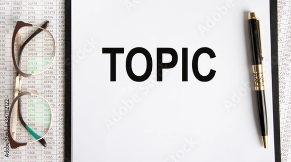 Obraz On the paper tablet is the inscription TOPIC, next to glasses and a pen, all against the background of accounting.