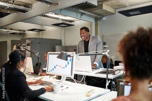 Obraz Smiling businessman discussing with young businesswoman over graph at office