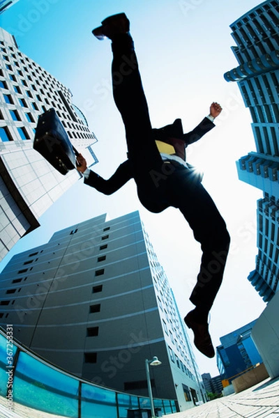 Obraz ビル街でジャンプするビジネスマン
