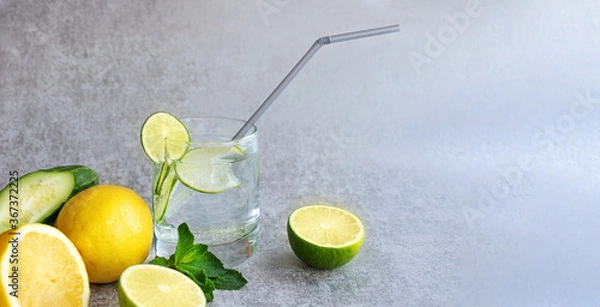 Obraz Refreshing lemonade in a clear glass with a straw, with lemon, lime, mint and fresh cucumber, on a gray background. Banner, selective focus, close-up, copy space