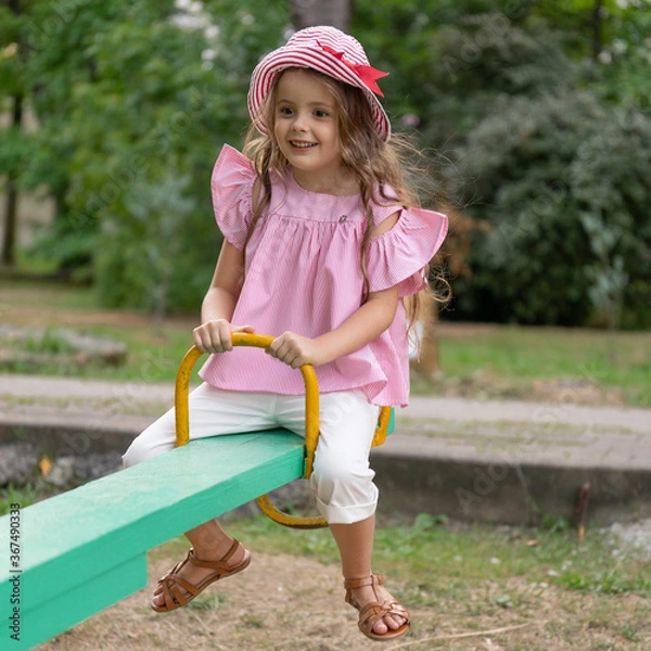 Obraz A child plays on the playground. Kid is riding on swings in the park. Charming little girl is having fun