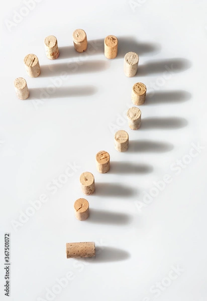 Fototapeta Wine bottle corks arranged to form a question mark on a white background.