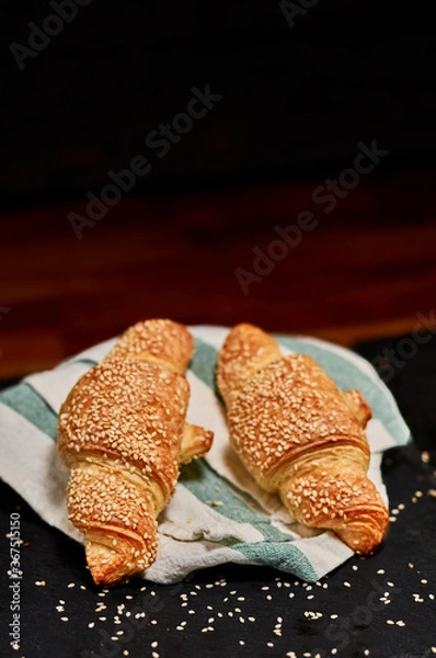 Fototapeta Freshly made rolled puffed pastry with sesame seeds on black stone cutting board. Very shallow depth of field