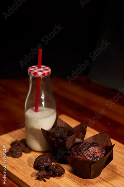Fototapeta Freshly made chocolate chip muffins with bottle of milk on wooden cutting board. Very shallow depth of field