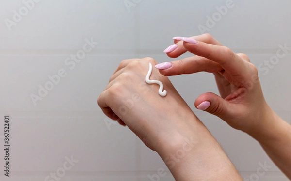 Fototapeta Close up of female hands applying moisturizing creme on the white tile background. Skincare and handcare concept. Cosmetic procedure.