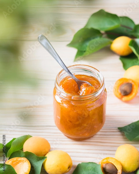Fototapeta Apricot jam in glass jar and ripe apricots on wooden rustic table, selective focus, vertical orientation
