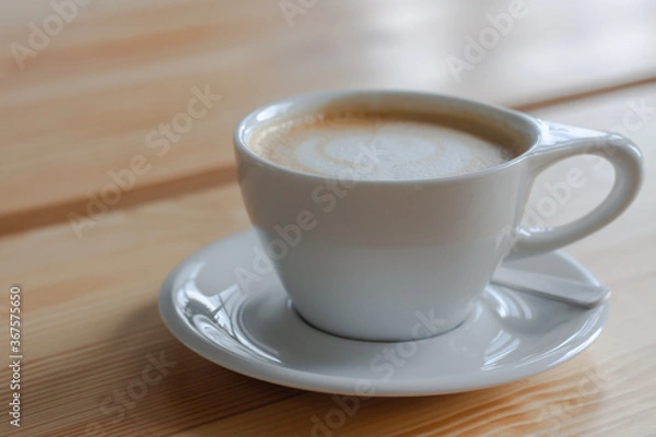 Fototapeta A white cup of coffee with foam on wooden background