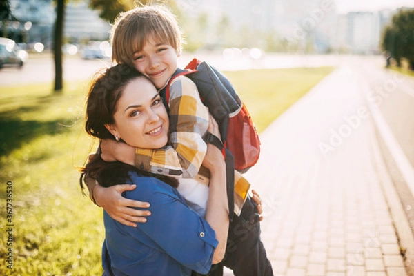 Fototapeta A mother hugs her young son on the way to school, and a mother and boy say goodbye before school. Concept of education and training, return to school
