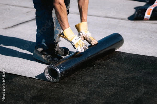 Fototapeta Professional workers waterproofing house construction site. Worker rolling membrane