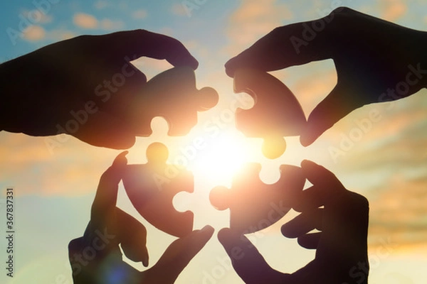 Fototapeta Four hands of businessmen put together a puzzle against the backdrop of a dramatic sky at sunset. Business concept idea, collaboration, teamwork, partnership, innovation