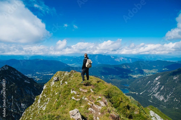 Obraz A tourist stands on top of a mountain with a backpack and looks into the distance. Trekking in the mountains.