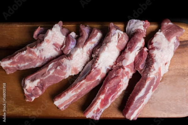 Fototapeta Close-up Raw Pork Ribs on a wooden board on a black background with free space for your text/decoration.