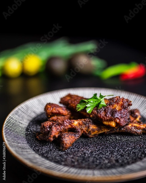 Fototapeta Close-up freshly made smoked glazed paprika Ribs in a serving plate with vegetables in the background. Concept of serving cooked rib meal.
