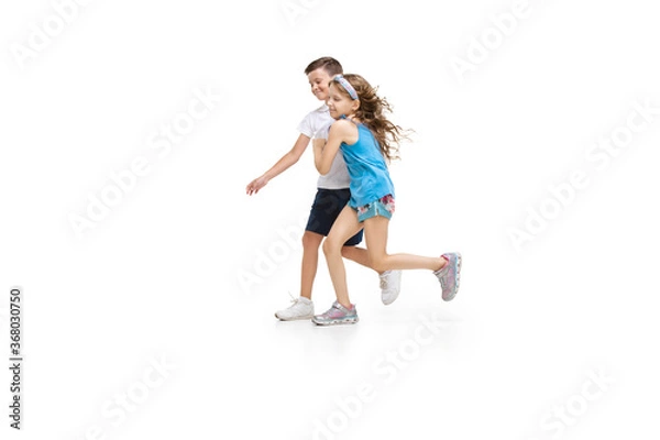 Obraz Happy kids, little and emotional caucasian boy and girl jumping and running isolated on white background. Look happy, cheerful, sincere. Copyspace for ad. Childhood, education, happiness concept.