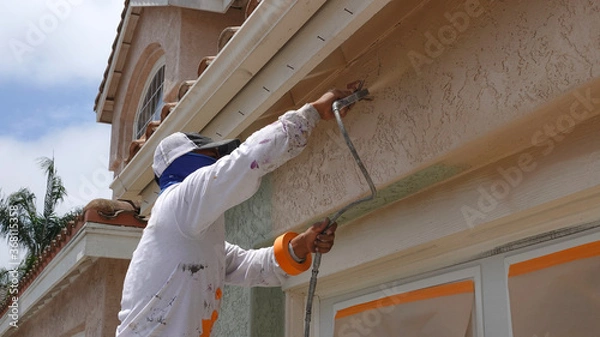 Fototapeta Professional contractor using a spray paint gun to paint the stucco on a home