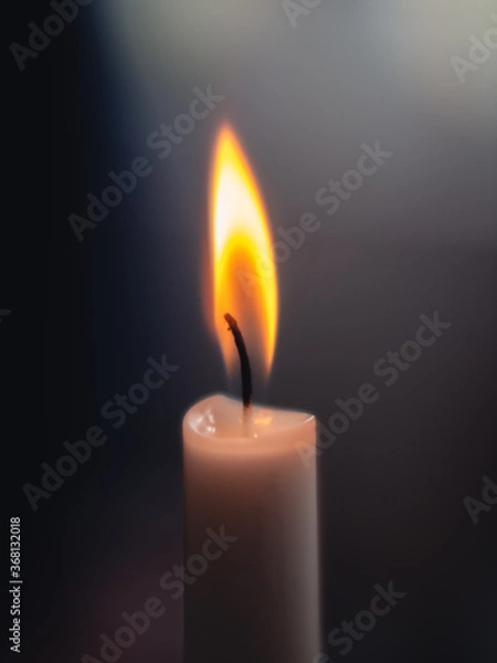 Fototapeta Close-up of a shining and glowing candle light with a warm flame and a blurry dark background
