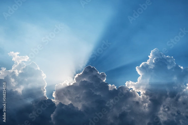 Obraz Sunbeams through a dark cumulus cloud in a blue sky