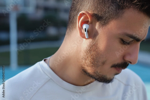 Obraz Bluetooth headphones on the ear of a young male person. 