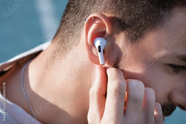 Obraz Bluetooth headphones on the ear of a young male person. 