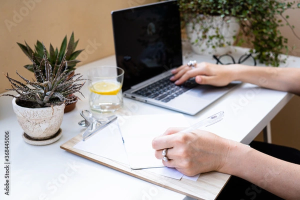 Fototapeta Woman's hands on laptop keyboard, writing in notepad
