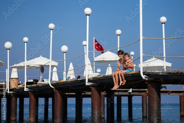 Obraz Two brothers sit on the pier and look at the sea