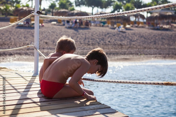 Obraz Two brothers sit on the pier and look at the sea