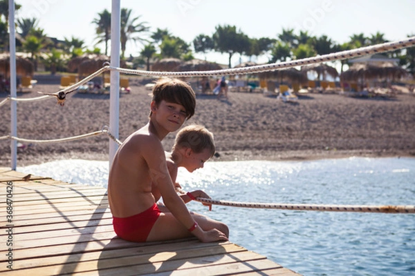 Obraz Two brothers sit on the pier and look at the sea