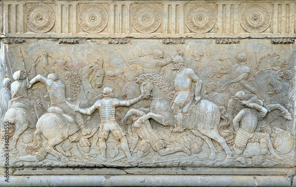 Fototapeta Ancient relief with the scene of a medieval war with knigts, engraved in white stone - background wallpaper