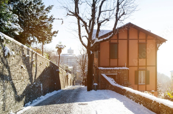Fototapeta A snow covered lane with a building and walls on either side,, and glimpses of a distant town