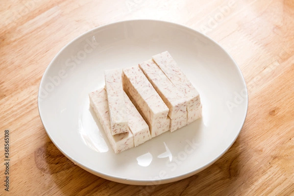 Fototapeta A dish of neatly cut taro pieces on a wood-grain table