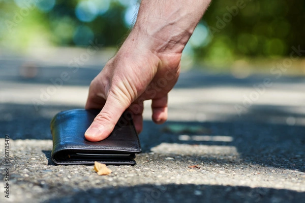 Fototapeta Photo of a sidewalk and the hand of a man who found a black wallet while walking