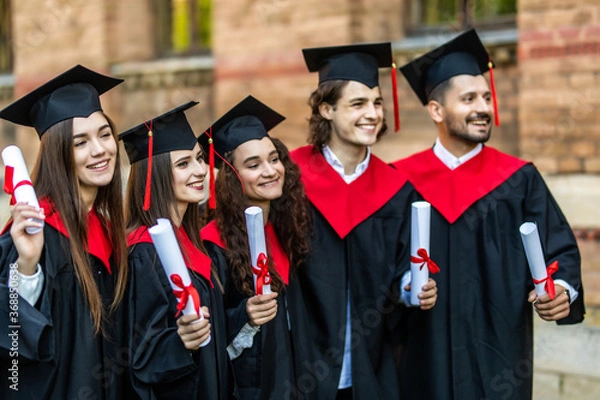 Fototapeta Successful excited five graduates in robes standing in row and showing certificate.
