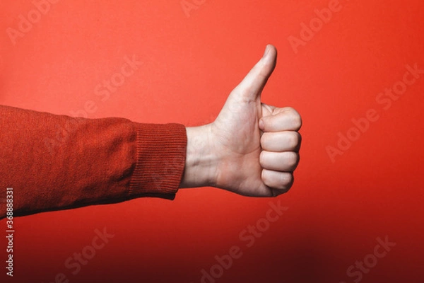 Fototapeta Man hand shows thumb up on red background.