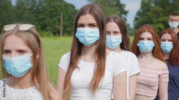 Fototapeta Pandemic concept. A group of students stand in a row in masks.