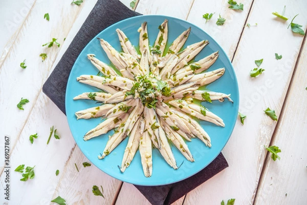 Fototapeta  Pickled anchovies with garlic and parsley marinated in vinegar in a round wooden plate on a white wooden table. Typical Spanish snack. 