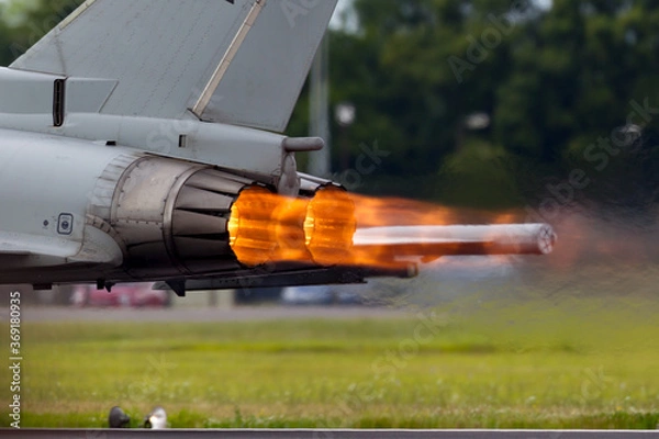 Obraz Afterburners glowing on an air force fighter jet aircraft as it speeds down the runway of an air base.