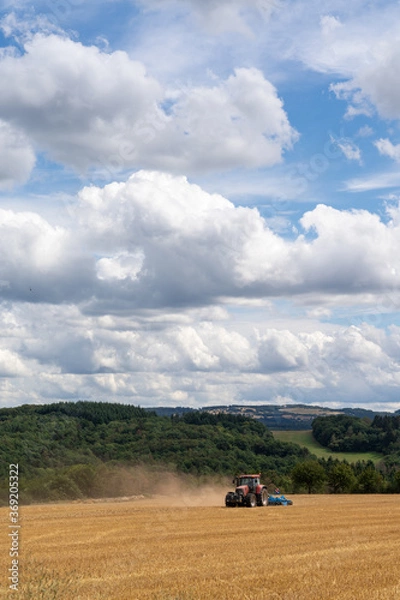 Fototapeta red tractor pulling a blue field cultivator across a harvested wheat field