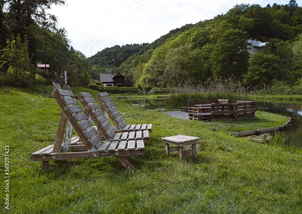 Obraz Ecological outdoor recreation, forest, lake, tables, loungers for relaxation, eco tourism background, beautiful natural scene, Cafe terrace in the mountains by the lake surrounded by forest.