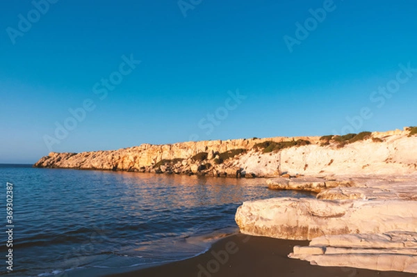 Fototapeta Deserted rocky seashore lit by the dawn sun