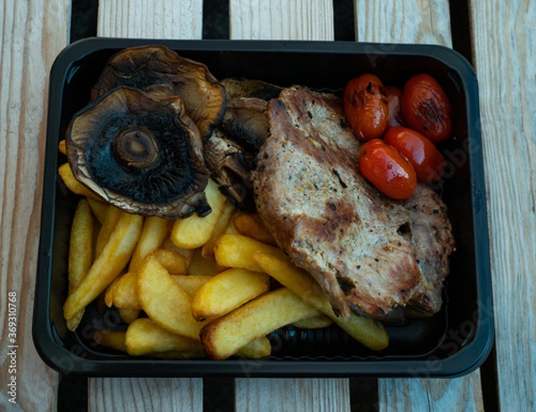Obraz Grilled street food closeup mushrooms, french fries, grilled fish, potato. Served in a plate, selective focus on a wooden table, background.