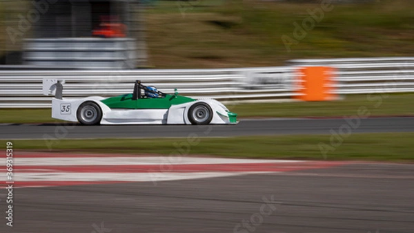 Fototapeta A panning shot of a white and green racing car as it circuits a track.