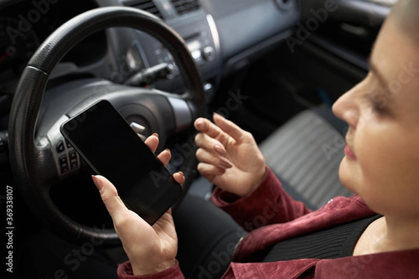 Obraz People, age, transportation, modern lifestyle and technolgy concept. High angle view of stylish gray haired mature woman sitting in driver's seat holding smart phone, setting online GPS navigation app