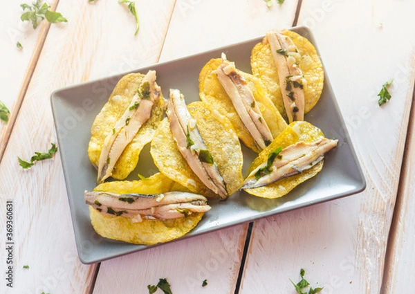 Fototapeta Potato chips with pickled anchovies in a dark rectangular plate on a white wooden table. Typical Spanish food to eat in a bar.