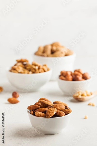 Fototapeta A handful of almonds in a white bowl, assorted nuts on a light background. Healthy snacks, healthy fats. Copy space.