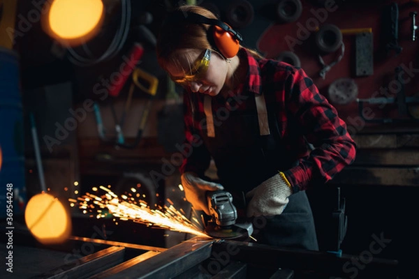 Fototapeta Woman working with angle grinder cuts and polishes metal after welding with spark